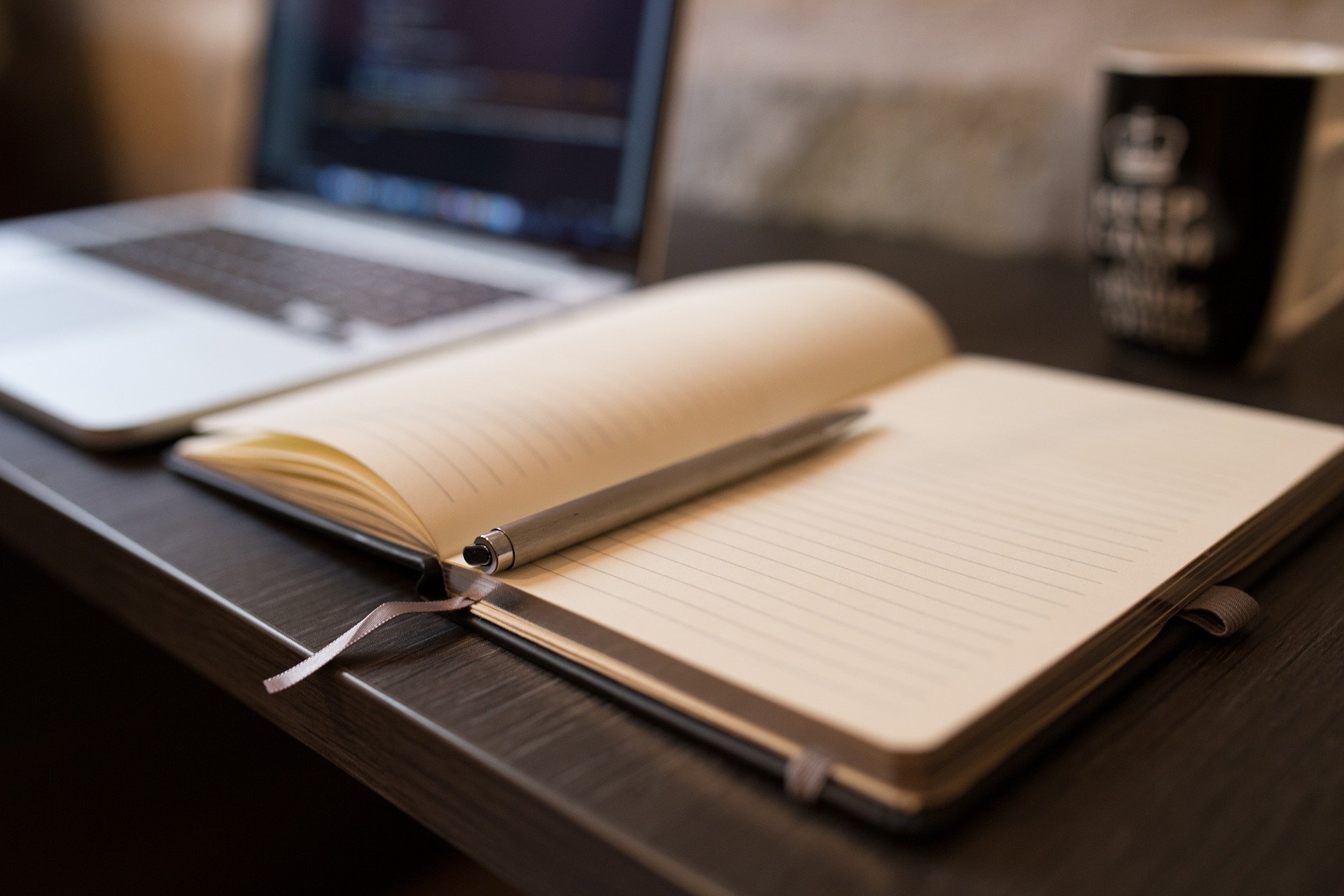 Buch mit Stift und Laptop auf dunklem Schreibtisch